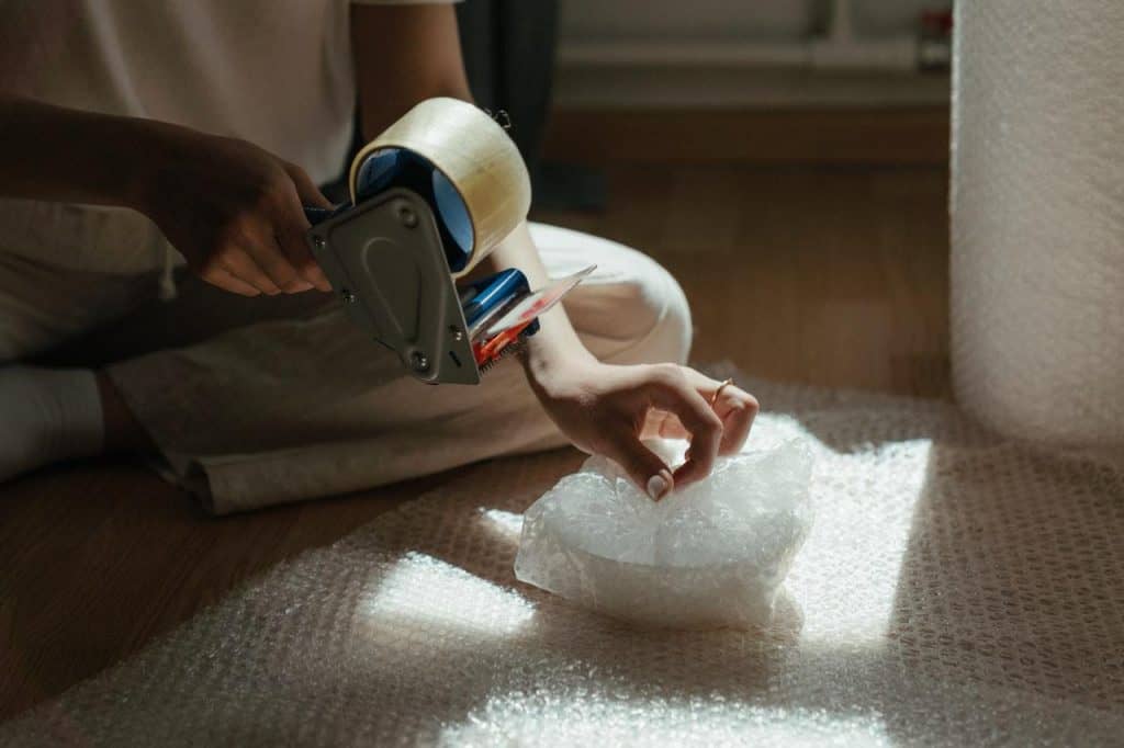 A woman sitting on the floor wrapping a bowl in bubble wrap.