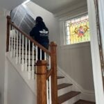 Blue Ox movers carrying a wrapped piece down a staircase past a stained-glass window